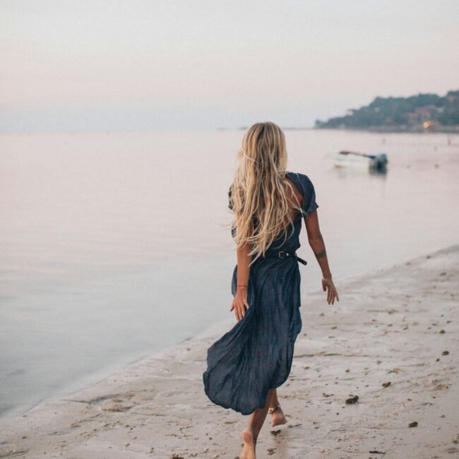 Femme de dos marchant au bord de la mer, symbole de cheminement personnel et de reconnection à soi.