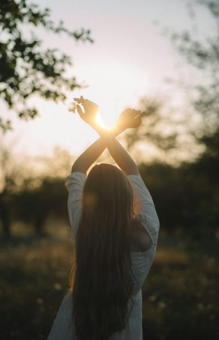 Femme levant les bras vers le ciel dans la lumière du soleil, symbole d’espoir et de renouveau